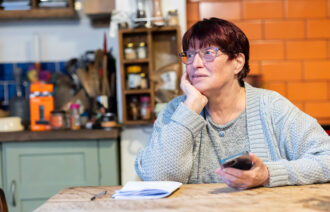 Woman sits at kitchen table holding phone.